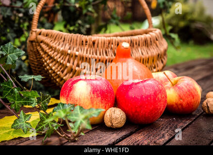 Herbst im Garten. Eine Komposition mit Äpfel, Kürbis und ein Korb mit Walnüssen Stockfoto