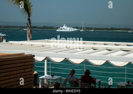 Ein Paar, das an einem Sommernachmittag in Ortigia, Sizilien, Italien, den Blick auf das Meer von einem gehobenen Restaurant mit Blick auf das Wasser genießt. Gute Küche. Luxus Stockfoto