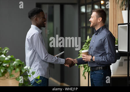 Zwei glückliche diverse männliche Kollegen handshaking stehen in modernen Büro Stockfoto