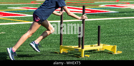 High School cros Land runner drückt eine schwere Schlitten über ein Rasenfeld suring Stärke Praxis. Stockfoto