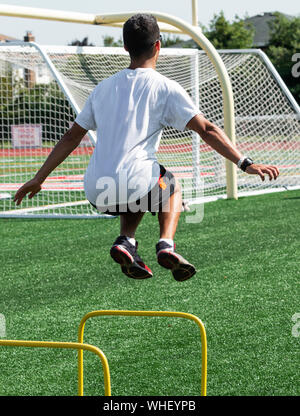 Ein High School Boy ist das Springen über zwei Fuß gelb Hürde bei der Leichtathletik Praxis auf grünen Rasen Stockfoto