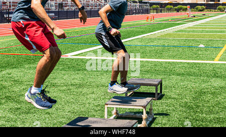 Zwei männliche High School Leichtathleten tun, springt auf grünem Rasen Feld während der Stärke und Beweglichkeit zu üben. Stockfoto