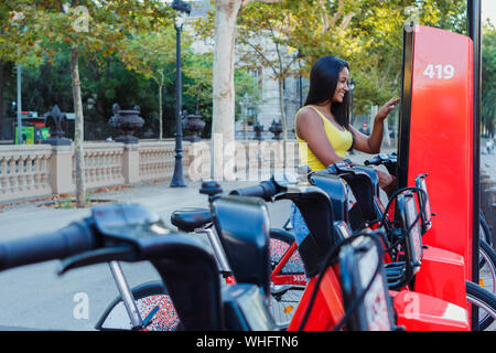 Latin Frau, ein Fahrrad in einem Fahrradverleih Plattform Stockfoto