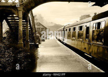 Schwarze und weiße retrospektive Foto einer Dampfeisenbahn und carraiges am Bahnhof Weybourne, Norfolk, England, UK, die Plattform ist neblig und in der d Stockfoto