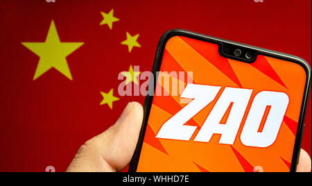 Hand hält ein Smartphone mit ZAO app Logo. Die unscharfen Flagge von China im Hintergrund. Zao ist derzeit einer Zahl eine unterhaltsame App in China. Stockfoto