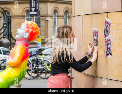 Oor Wulie Zeichentrickfigur schaufel Art Trail & junge Frau buchung Flyer an der Wand des Nationalen Museums während Fringe Festival, Edinburgh, Schottland, Großbritannien Stockfoto