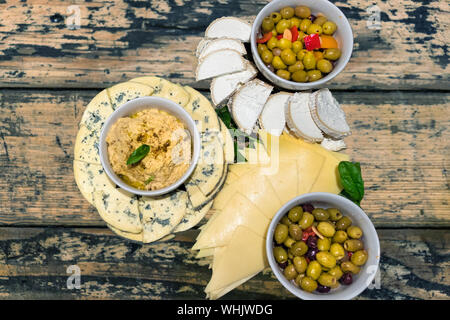 Snack Platten mit Humus und Oliven auf Schalen gelegt und Blauschimmelkäse auf einem Holztisch in Scheiben geschnitten, Ansicht von oben. Stockfoto