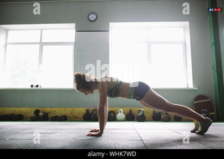 Ein schönes Mädchen ist Push-ups aus dem Boden für das Training der Muskeln der Hände, Rücken und Prema in der Turnhalle auf dem Hintergrund des Lichts windows Stockfoto