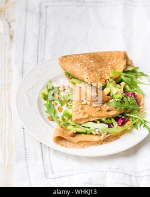 Vertikale selektive Nahaufnahme von dreieckigen Pfannkuchen mit Gemüse und Muttern auf einer weißen Platte Stockfoto