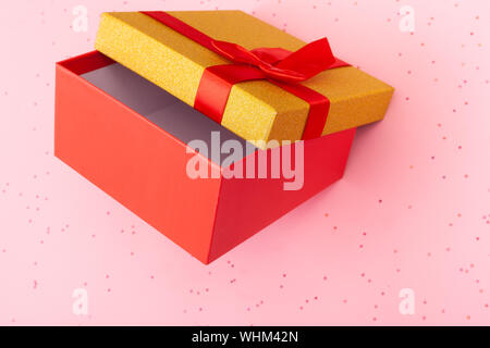 Rote Geschenkbox mit Deckel mit einem Bogen auf einem rosa Hintergrund. Glitzer Hintergrund. Stockfoto