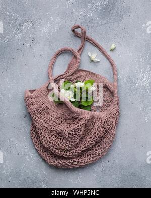 Vertikale Nahaufnahme von weißen Blüten mit grünen Blättern auf Eine dunkelstaubige rosa Stricktasche Stockfoto