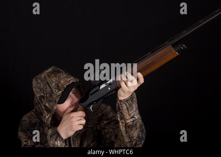 Der Mann mit dem Gewehr zielt. Hunter in der Tarnung Kleidung mit einer Schrotflinte auf einem schwarzen Hintergrund. Militär mit Waffen. Kopieren Sie Platz. Vorbereitung für Autolöscher Stockfoto