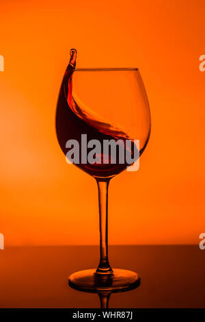 Ein Glas Wein mit einem Schuss Wein auf einem gelben Hintergrund. Ein Glas auf der Theke in einem Cafe, Restaurant, Disco oder Disco. Stockfoto