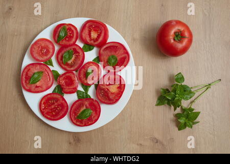 Direkt über der in Scheiben geschnittene Tomaten mit Basilikum auf der Platte gegen die hölzernen Hintergrund Stockfoto