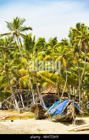 Atemberaubende Aussicht auf einen Strand mit einem hölzernen Boot vor einem Fischerdorf, umgeben von wunderschönen Palmen umgeben. Cochin, Kerala, Indien. Stockfoto