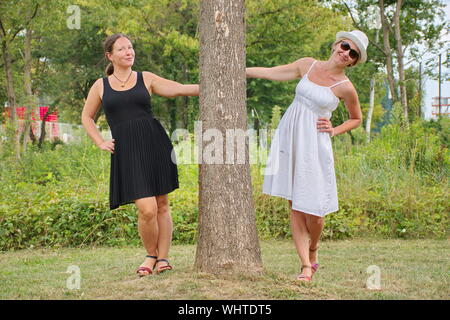 Porträt der jungen Frauen mit weißen und schwarzen Kleid posiert mit dem Baum im Park Stockfoto