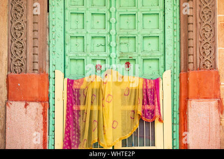 Atemberaubende Aussicht auf einer traditionellen indischen Home mit einem grünen Holztür und bunte traditionelle indische Kleidung (Sari) hängend trocknen. Stockfoto