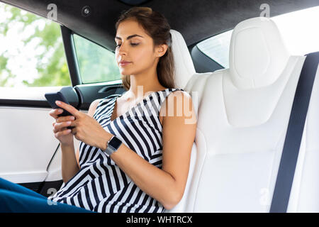 Geschäftsfrau eingeben Nachricht auf dem Telefon im Auto sitzen Stockfoto