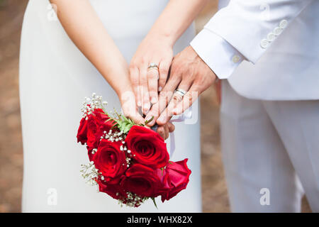 Frisch verheiratete Ehepaar vergleichen Ihre Hochzeit Ringe halten an den Händen und einem Blumenstrauß. Stockfoto