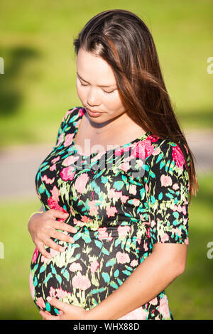 Schwangere Frau in blumigen Shirt sieht auf den schwangeren Bauch mit einem Sommer Hintergrund Stockfoto