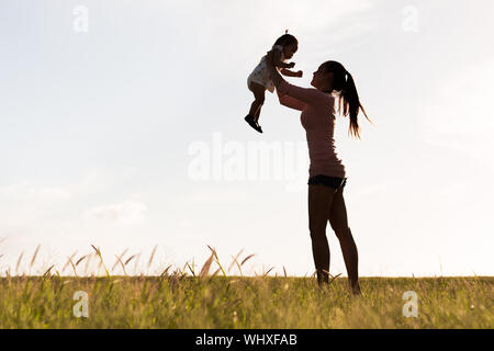 Silhouette einer Mutter und ihrem kleinen Kind spielen in einem goldenen Wiese Stockfoto