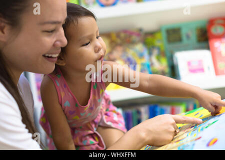 Mutter und Kind sind auf der Suche nach Bilder in einem großen Buch beim Einkaufen in einer Buchhandlung. Stockfoto