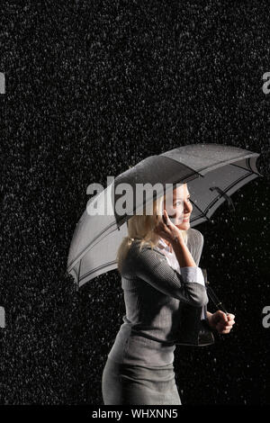 Seitenansicht eines lächelnden Geschäftsfrau mit Handy unter dem Dach bei Regen Stockfoto