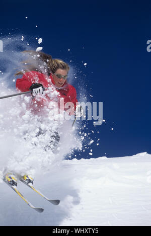 Skifahrerin Skiing durch Pulverschnee auf der Piste gegen den klaren blauen Himmel Stockfoto