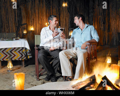 Zwei Männer mit Lagerfeuer im Freien Nachtclub sitzen Toasten Stockfoto