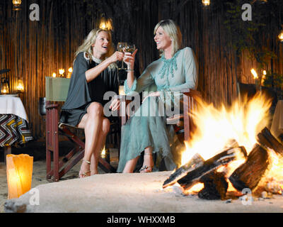 Zwei Frauen durch Lagerfeuer im Freien Nachtclub sitzen Toasten Stockfoto