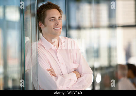Happy Geschäftsmann mit verschränkten Armen lehnte sich auf Büro Glastür Stockfoto