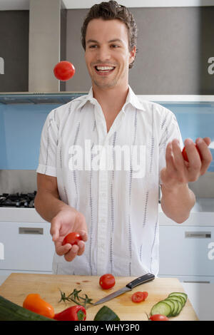 Fröhlicher junge Mensch jonglieren Tomaten während der Zubereitung von Speisen in der Küche Stockfoto