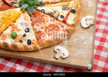 Pizza verschiedene Stücke auf einem Board auf einem karierten Tischtuch mit Pilzen dekoriert und Basilikum Stockfoto