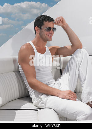 Lächelnden jungen Mann mit Sonnenbrille beim Sitzen auf einem Sofa in Yacht Stockfoto