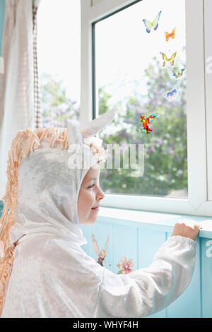 Profil eines lächelnden jungen Mädchen in Einhorn Kostüm an künstlichen Schmetterlinge suchen im Fenster Stockfoto