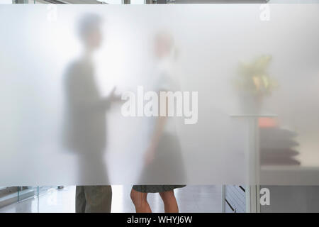 Seitenansicht eines männlichen Büroangestellter im Gespräch mit weiblichen Kollegen hinter durchsichtigen Wand im Büro Stockfoto