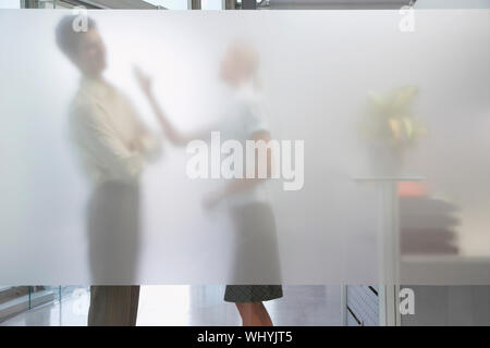 Seitenansicht eines weiblichen Büroangestellten argumentieren mit männlichen Kollegen hinter durchsichtigen Wand im Büro Stockfoto