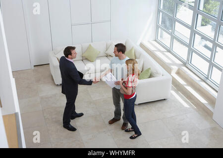 Ansicht eines männlichen Immobilienmakler Händeschütteln mit einem Mann von Frau im neuen Zuhause Stockfoto