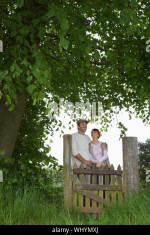 Nachdenklich Paar stehend über Feld Tor unter den Baum. Stockfoto