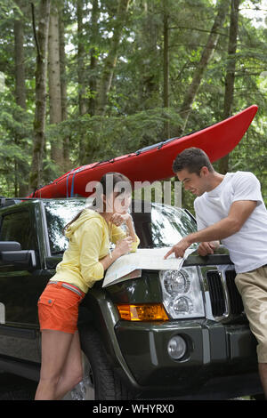 Seitenansicht eines jungen Paares auf Karte auf der Motorhaube im Wald suchen Stockfoto