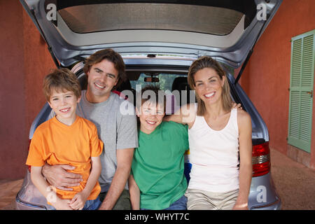 Portrait eines glücklichen Paar mit zwei Söhne sitzen auf Auto Heckklappe Stockfoto