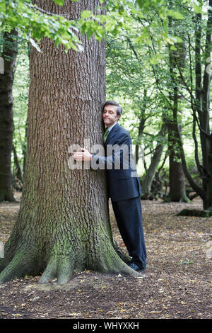 Volle Länge des Geschäftsmannes umarmt Baum im Wald Stockfoto