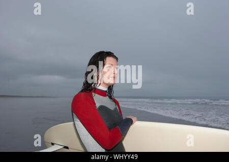 Schöne weibliche Surfer mit Surfbrett weg schauen am Strand Stockfoto