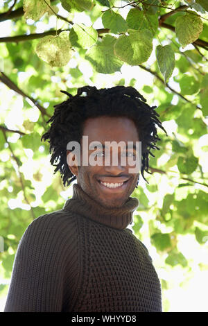 Porträt der glückliche junge afrikanische amerikanische Mann mit Pullover stehen im Park Stockfoto