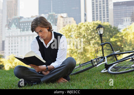 Volle Länge des hübscher junger Geschäftsmann lesen Buch mit dem Fahrrad in Park Stockfoto