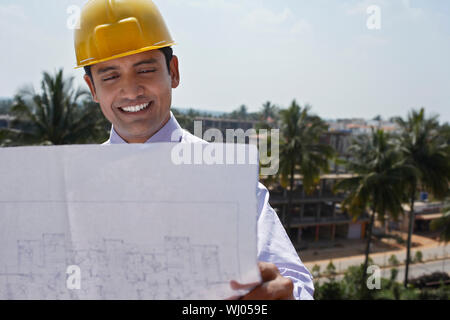 Glückliche junge Geschäftsmann, tragen, Hardhat, während bei Blueprint im Freien suchen Stockfoto