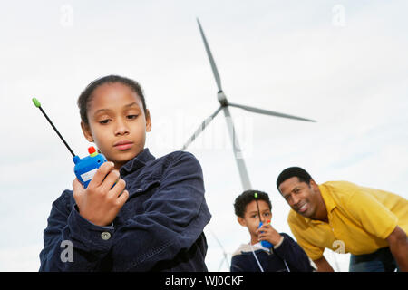 Vater und Kinder (7-9) spielen mit Walkie-Talkies im Windpark Stockfoto