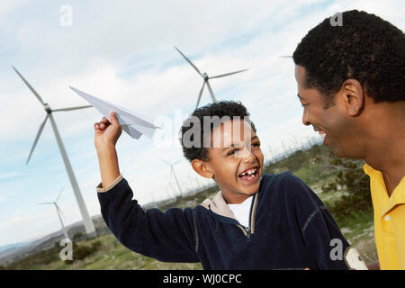 Vater und Sohn (7-9) spielen mit Papierflieger im Windpark Stockfoto