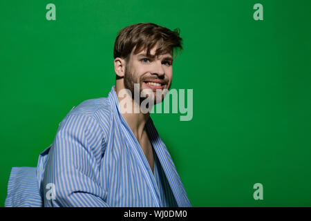 Home Kleidung, Freizeitbekleidung. Gerne macho mit bärtigen Gesicht im Bademantel. Mann in blauen Morgenmantel auf grünem Hintergrund. Spa, Wellness, Pflege. Mode Stockfoto