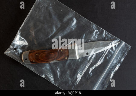 Messer in einem Kunststoffgehäuse auf Schwarz Farbe Hintergrund Tabelle. Physische beweise Pack. Kriminelle Konzept. Stockfoto